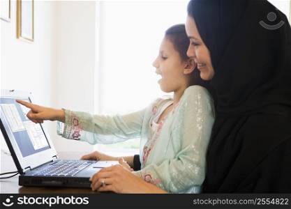 Mother and daughter in office with laptop pointing and smiling (high key/selective focus)