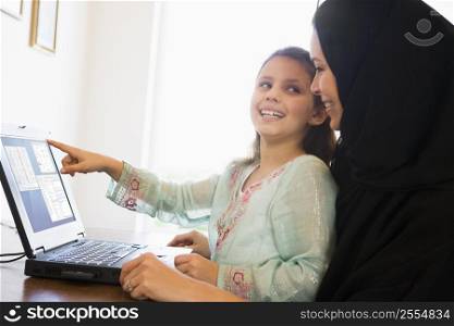 Mother and daughter in office with laptop pointing and smiling (high key/selective focus)