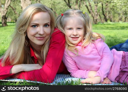 Mother and daughter in park lie on grass in spring