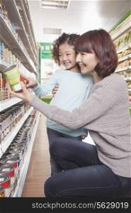 Mother and Daughter in Supermarket Shopping, Kneeling and Looking at a Product