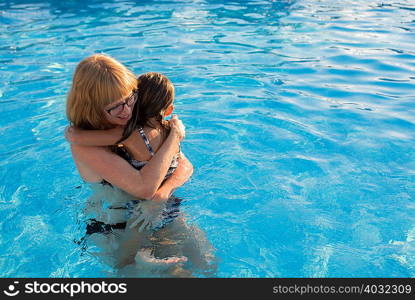 Mother and daughter in swimming pool, hugging