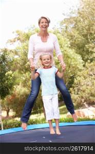 Mother And Daughter Jumping On Trampoline In Garden