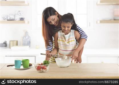 Mother and daughter kneading dough together in kitchen