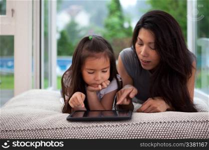 Mother and daughter laying on couch playing with a digital tablet