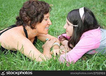 mother and daughter lie on the grass and look at each other