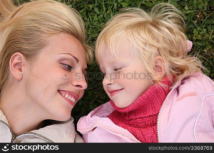 mother and daughter lie on the grass and look at each other