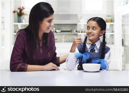 Mother and daughter looking at each other while girl having breakfast