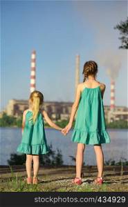 mother and daughter looking at the plant chimney-stacks polluting an air