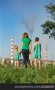 mother and daughter looking at the plant chimney-stacks polluting an air