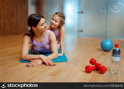 Mother and daughter lying on mat together in gym, fitness workout, gymnastic. Mom and little girl in sportswear, joint training in sport club. Mother and daughter lying on mat together in gym