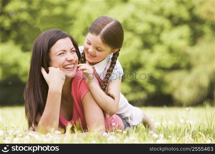 Mother and daughter lying outdoors with flower smiling