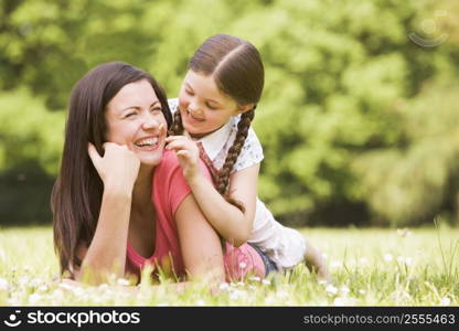 Mother and daughter lying outdoors with flower smiling