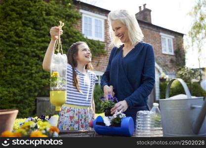 Mother And Daughter Making Recycled Plant Holders From Plastic Bottle Packaging Waste In Garden At Home