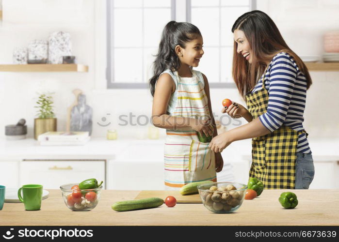 Mother and daughter making vegetable salad in kitchen