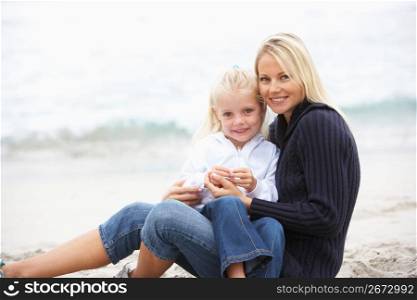 Mother And Daughter On Holiday Sitting On Winter Beach