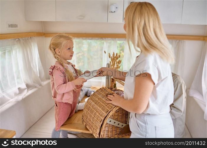 Mother and daughter on the kitchen in trailer, summer camping. Couple with kids travel in camp car, motorhome interior on background. Campsite adventure, travelling lifestyle, vacation on rv vehicle. Mother and daughter on kitchen in trailer, camping