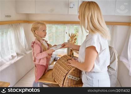 Mother and daughter on the kitchen in trailer, summer camping. Couple with kids travel in camp car, motorhome interior on background. Campsite adventure, travelling lifestyle, vacation on rv vehicle. Mother and daughter on kitchen in trailer, camping