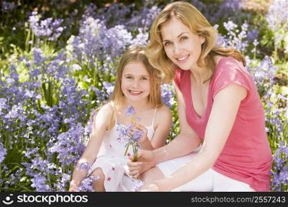 Mother and daughter outdoors holding flowers smiling