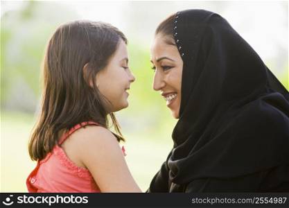 Mother and daughter outdoors in park embracing and smiling (selective focus)