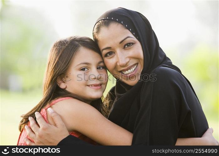 Mother and daughter outdoors in park embracing and smiling (selective focus)