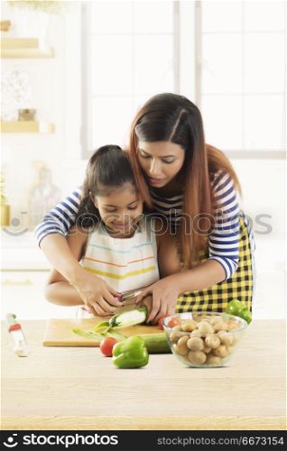 Mother and daughter peeling cucumber in kitchen