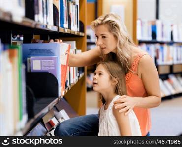 Mother and daughter picking a book in public library. That is a difficult choice