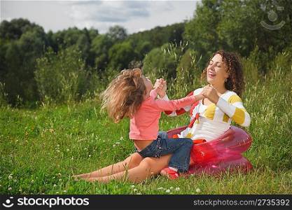 mother and daughter play in the open air, sitting on an inflatable armchair. take hands and smiling