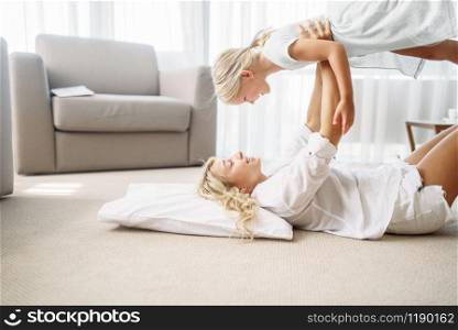 Mother and daughter play together lying on the floor at home. Parent feeling, togetherness, happy family