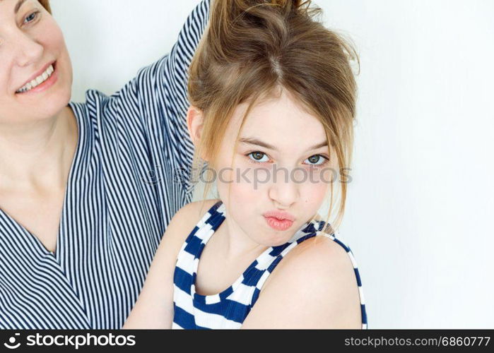 Mother and daughter playing with blond long hair near white wall