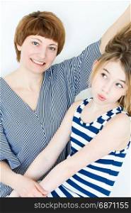 Mother and daughter playing with blond long hair near white wall