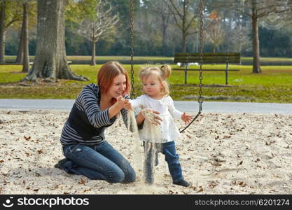 Mother and daughter playing with sand having fun at the park playground