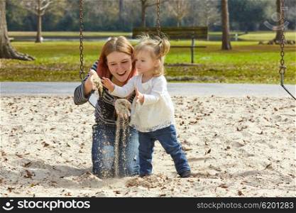 Mother and daughter playing with sand having fun at the park playground