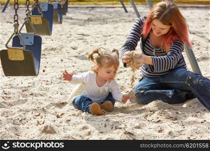 Mother and daughter playing with sand having fun at the park playground