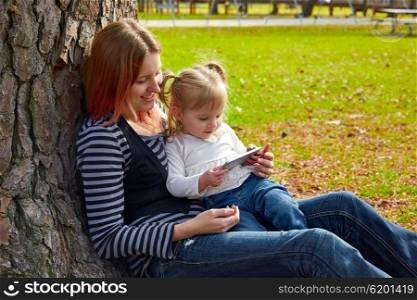 mother and daughter playing with smartphone together sitting in the park tree