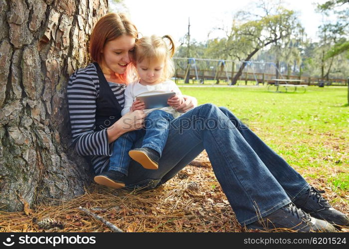 mother and daughter playing with smartphone together sitting in the park tree