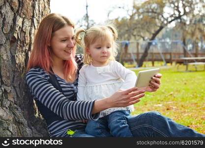 mother and daughter playing with smartphone together sitting in the park tree