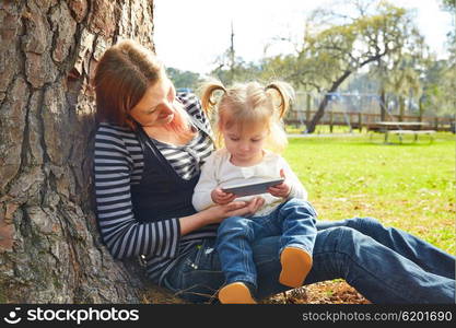 mother and daughter playing with smartphone together sitting in the park tree