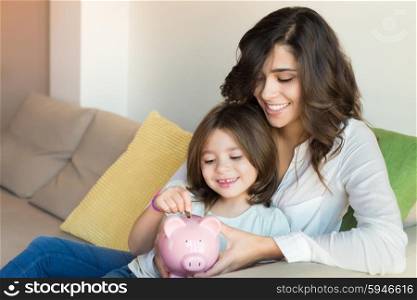 Mother and daughter putting coins into piggy bank