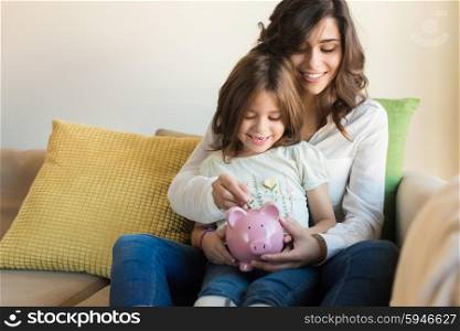 Mother and daughter putting coins into piggy bank