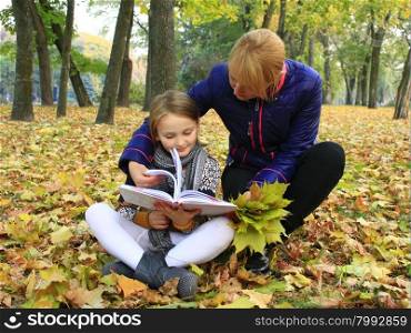 mother and daughter read a book in the autumn park. mother and her daughter read a book in the autumn city park