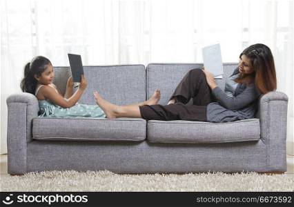Mother and daughter reading book on sofa