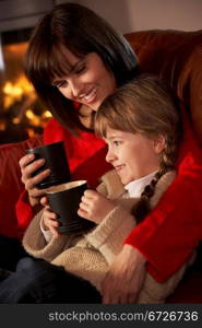 Mother And Daughter Relaxing With Hot Drink Watching TV By Cosy Log Fire