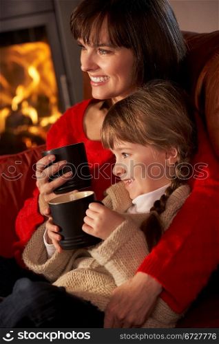 Mother And Daughter Relaxing With Hot Drink Watching TV By Cosy Log Fire