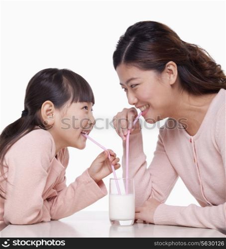 Mother and daughter sharing a glass of milk, studio shot