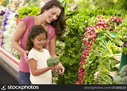 Mother and daughter shopping for broccoli at a grocery store