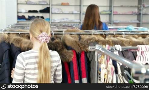 Mother and daughter shopping for girls clothes in a clothing store, child looking warmest jacket