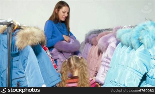 Mother and daughter shopping for winter clothes in a clothing store, child trying on down-padded coat