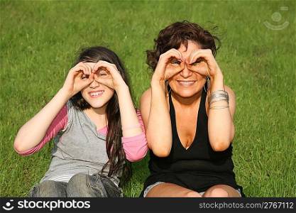 mother and daughter sit on the grass and look forward