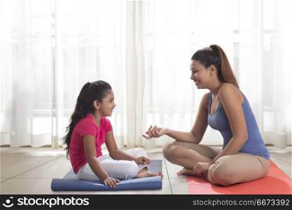 Mother and daughter sitting on exercise mat
