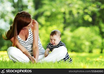 Mother and daughter sitting on grass in spring park